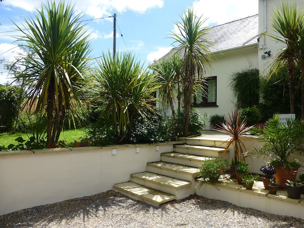 A staircase leading to a building with a white exterior, surrounded by various potted plants and a gravel area.