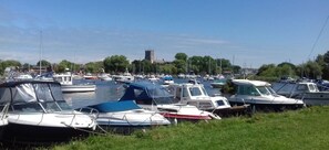 A marina with various boats docked, a grassy foreground, and a church in the background.