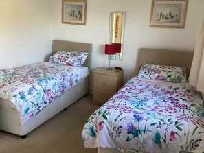 Two single beds with floral bedding, a bedside table with a lamp, and two framed pictures on the wall.