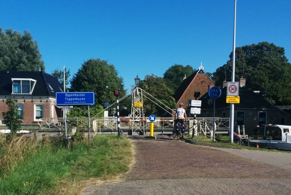 Un paso de tren con un ciclista, un puente y un edificio que dice 'Oppenhuizen'.
