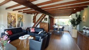 A spacious living area with a dark leather sofa, a coffee table, and a dining table with chairs. A wooden staircase leads to an upper level.