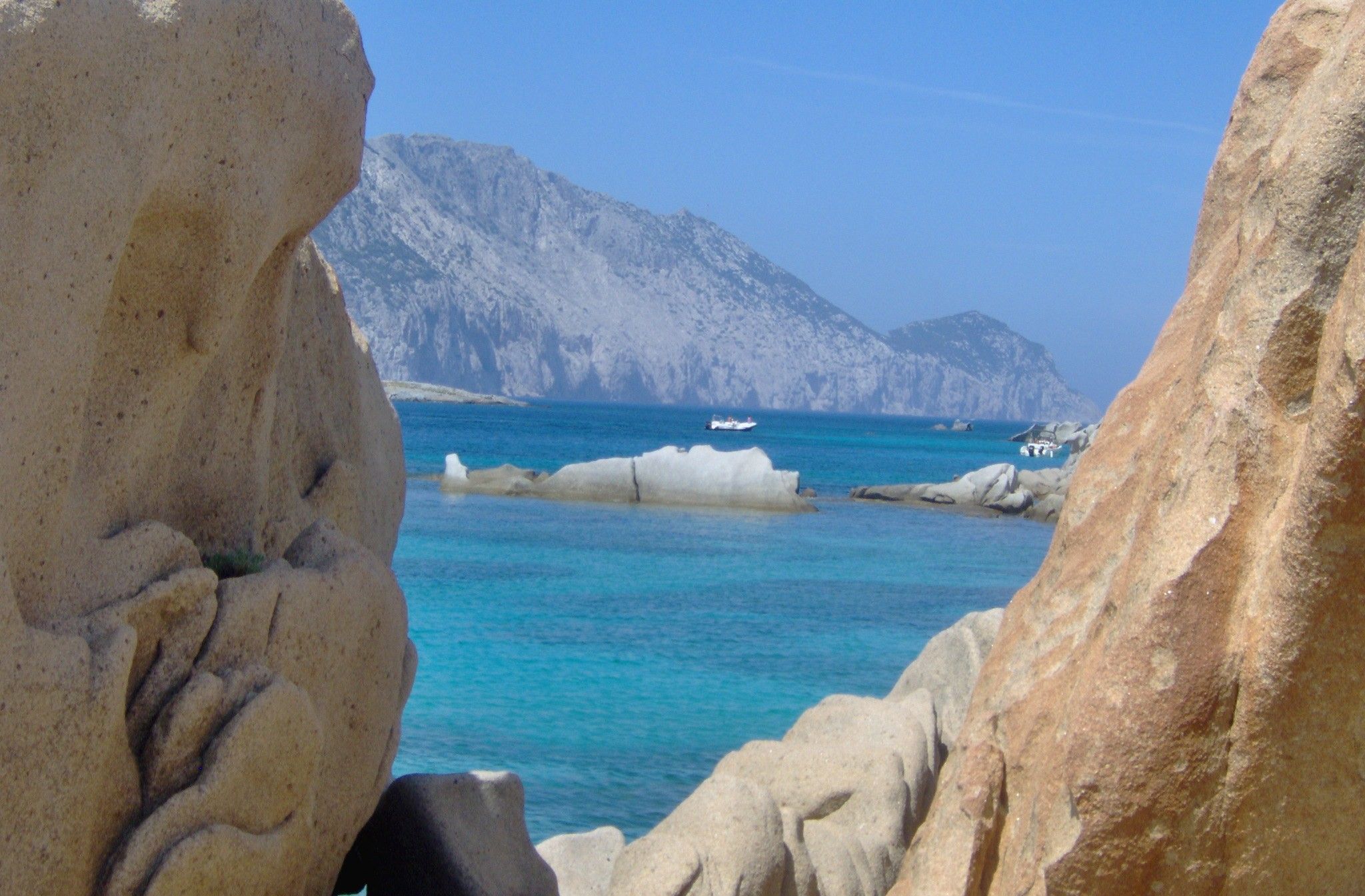 A rocky coastline with clear blue waters and distant mountains.