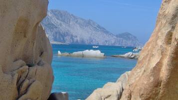 A rocky coastline with clear blue waters and distant mountains.