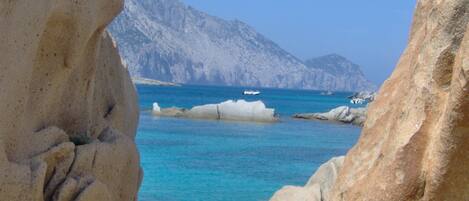 A rocky coastline with clear blue waters and distant mountains.