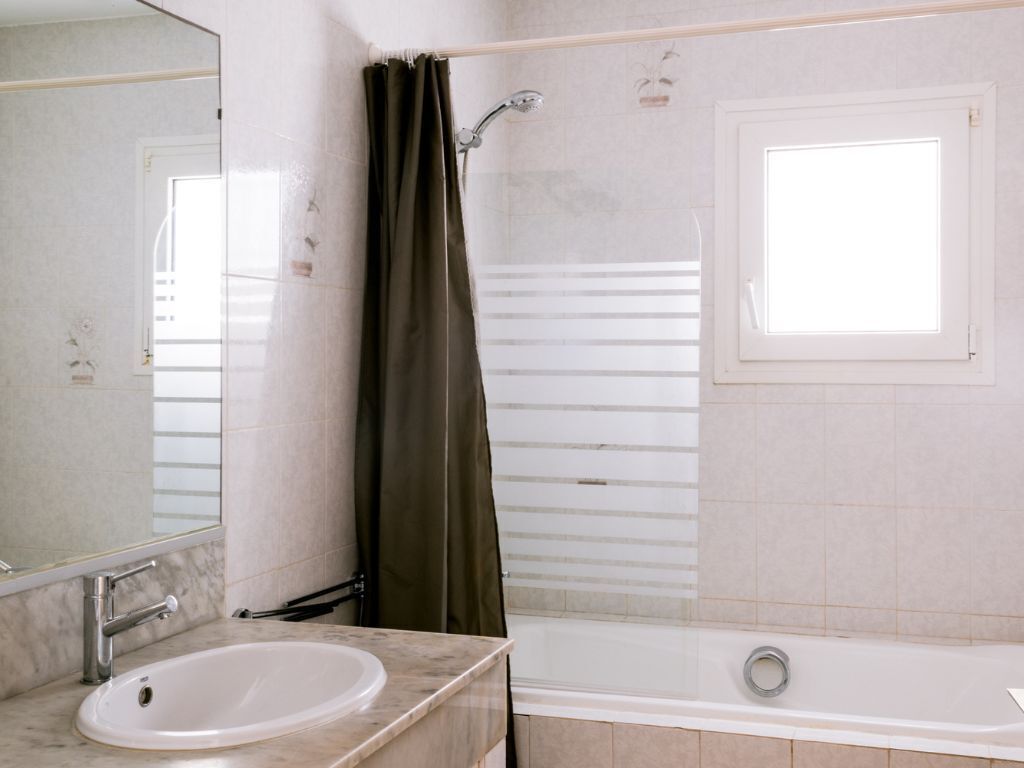 A bathroom with a white sink, a mirror, a shower curtain, a bathtub, and a window.