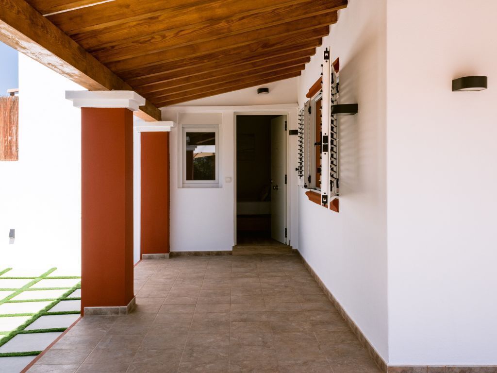 A corridor with a wooden ceiling, white walls, and a tiled floor.