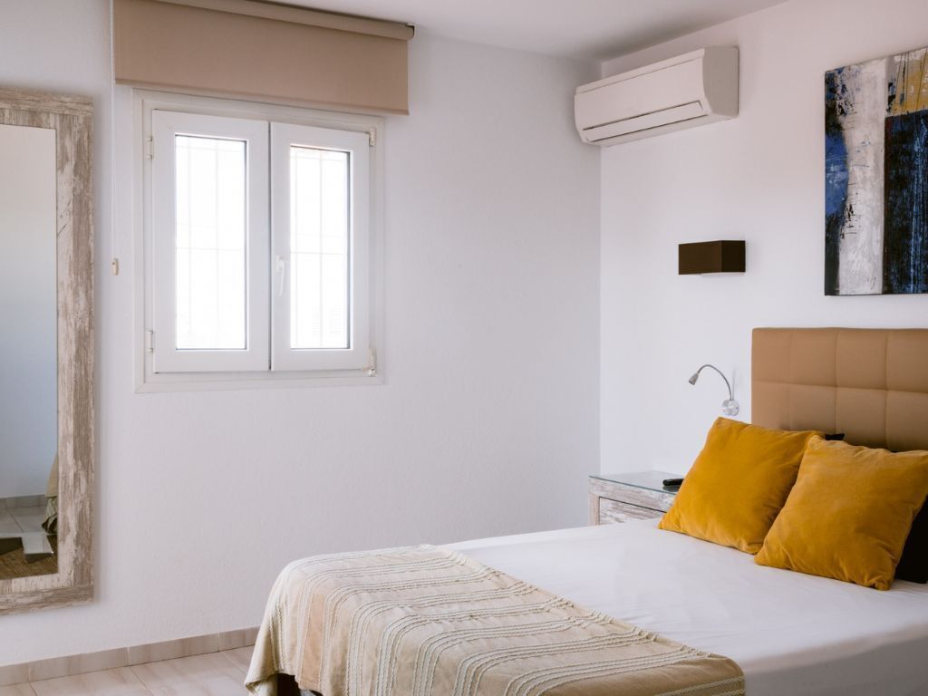 A bedroom with a bed, a nightstand, a mirror, and a window.