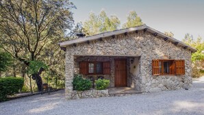 Una casa de piedra con puerta y ventanas de madera, rodeada de árboles y grava.