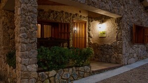 Un edificio de piedra con puerta de madera, banco, letrero iluminado y camino de piedra.