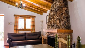 Una sala de estar acogedora con chimenea de piedra, vigas de madera en el techo, un sofá de cuero y una ventana con cortinas.