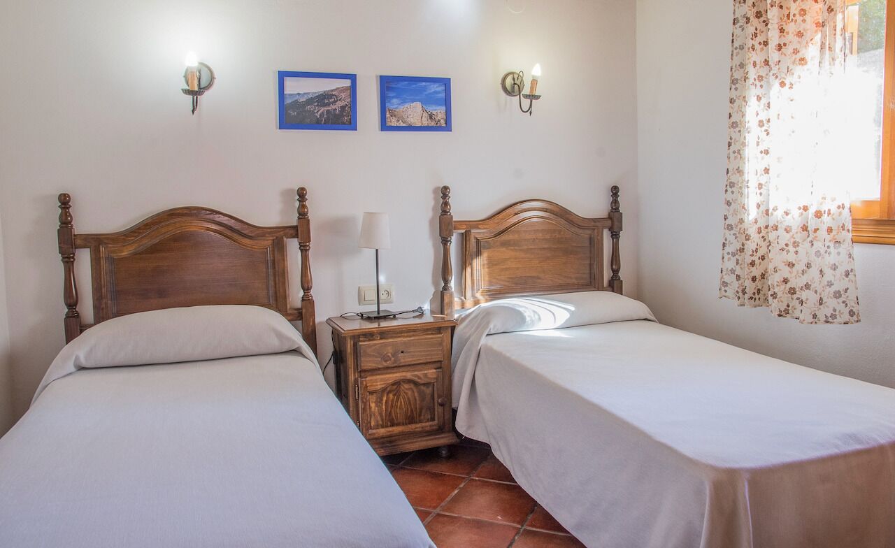 A room with two wooden beds, a nightstand with a lamp, and two framed pictures on the wall.