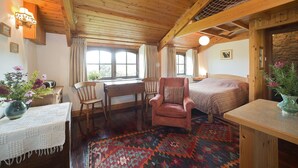 A cozy room with a wooden ceiling, a bed, a chair, a desk, and a window with curtains. - Cosy Cottage. Log Stove, Private Walled Garden, Coastal Walking From The Door. (St Davids)