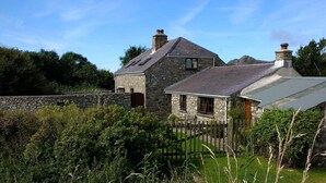 A stone house with a sloped roof, a wooden fence, and a stone wall in the background. - Cosy Cottage. Log Stove, Private Walled Garden, Coastal Walking From The Door. (St Davids)