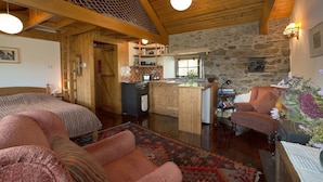 A cozy cabin interior with a wooden ceiling, stone walls, a kitchen area, and a seating area with a patterned rug. - Cosy Cottage. Log Stove, Private Walled Garden, Coastal Walking From The Door. (St Davids)