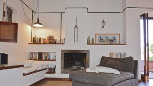 A cozy bedroom with a bed, a fireplace, shelves with books and decorative items, and a view of the outdoors. - House with pool, sea views near Cefalu and Castelbuono and beach 10 minutes (Pollina)