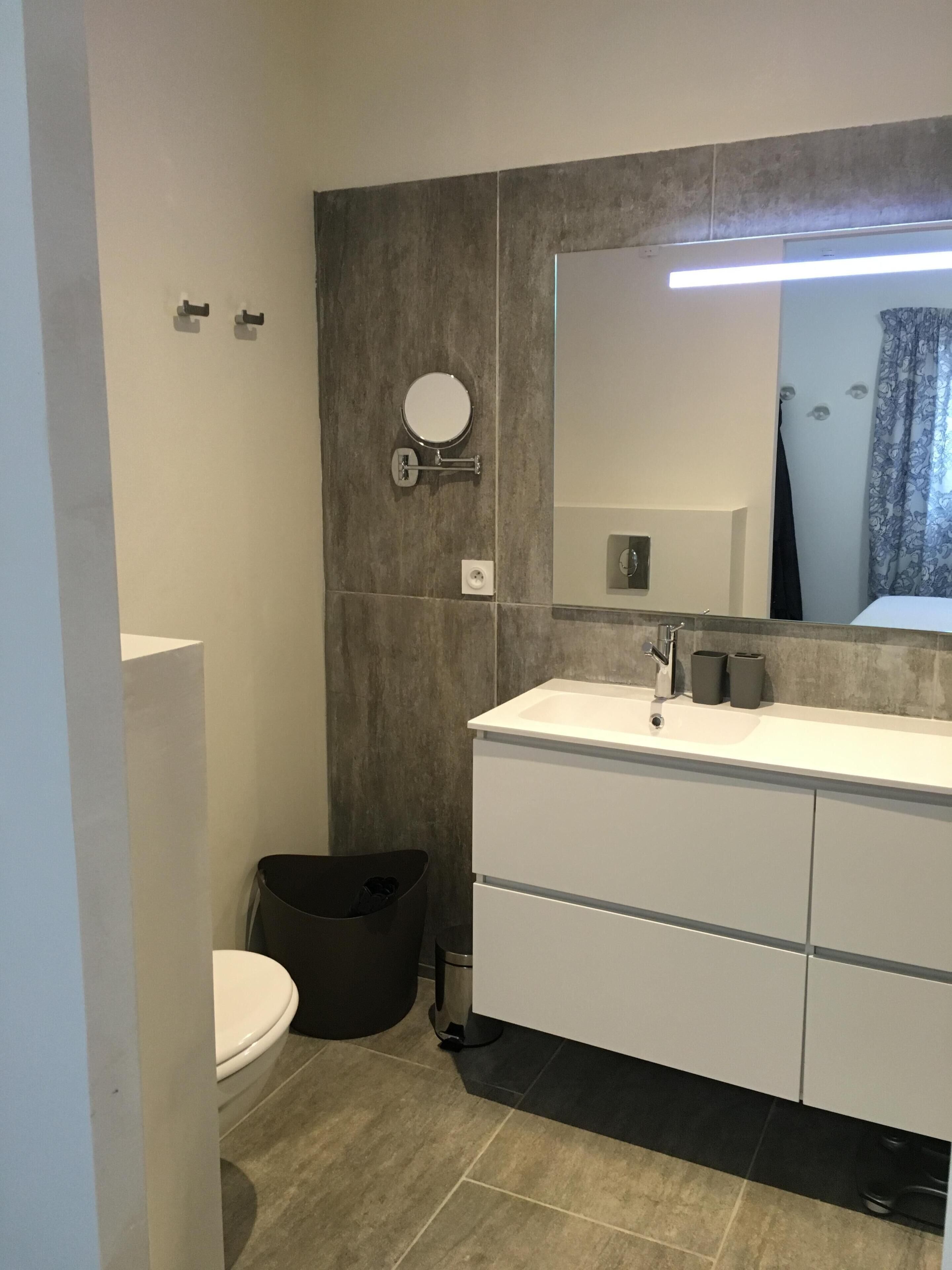A modern bathroom with a white sink, a round mirror, and a toilet.