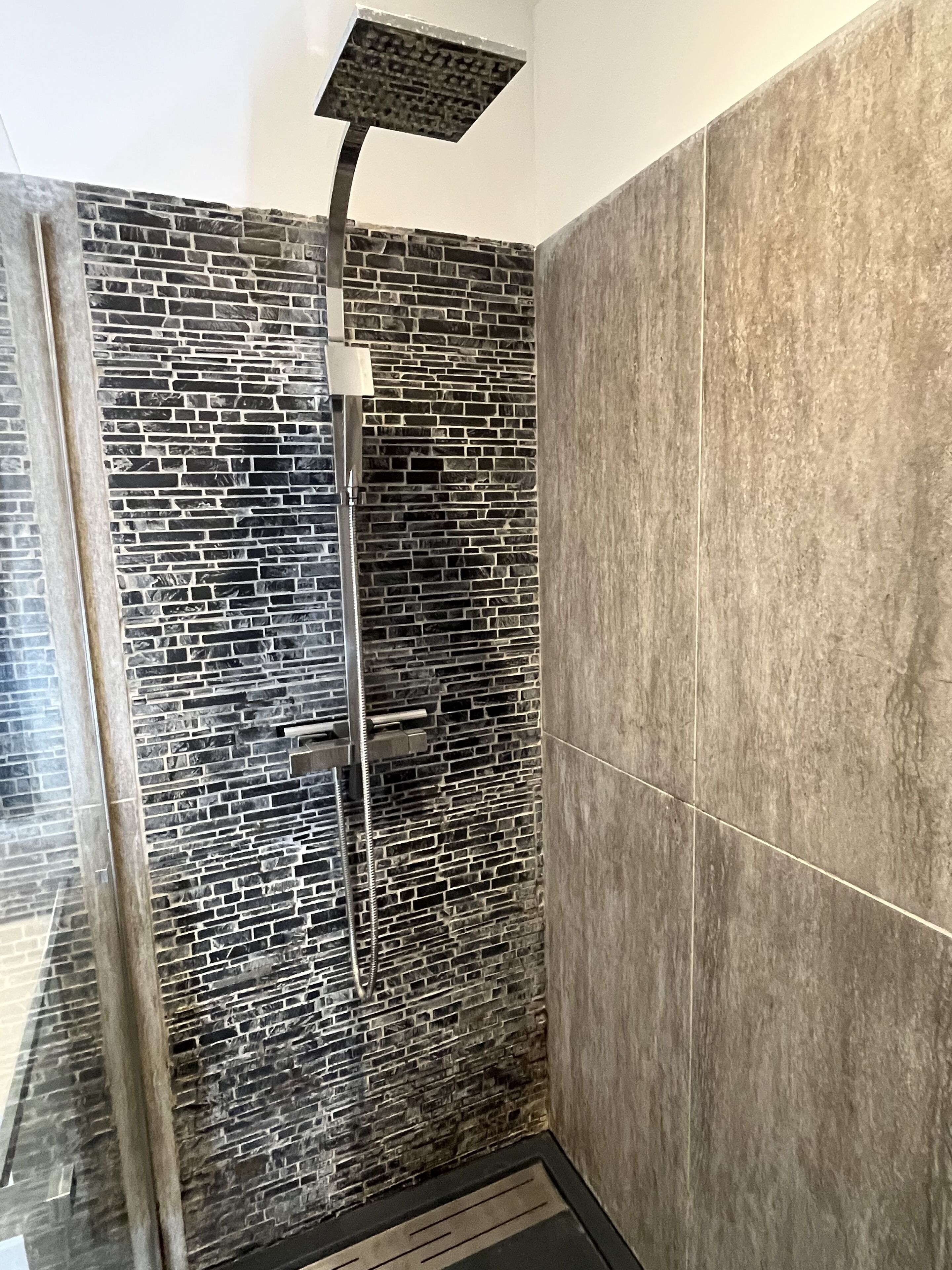 A shower with a modern design, featuring a stone-like wall and a sleek, metallic showerhead.