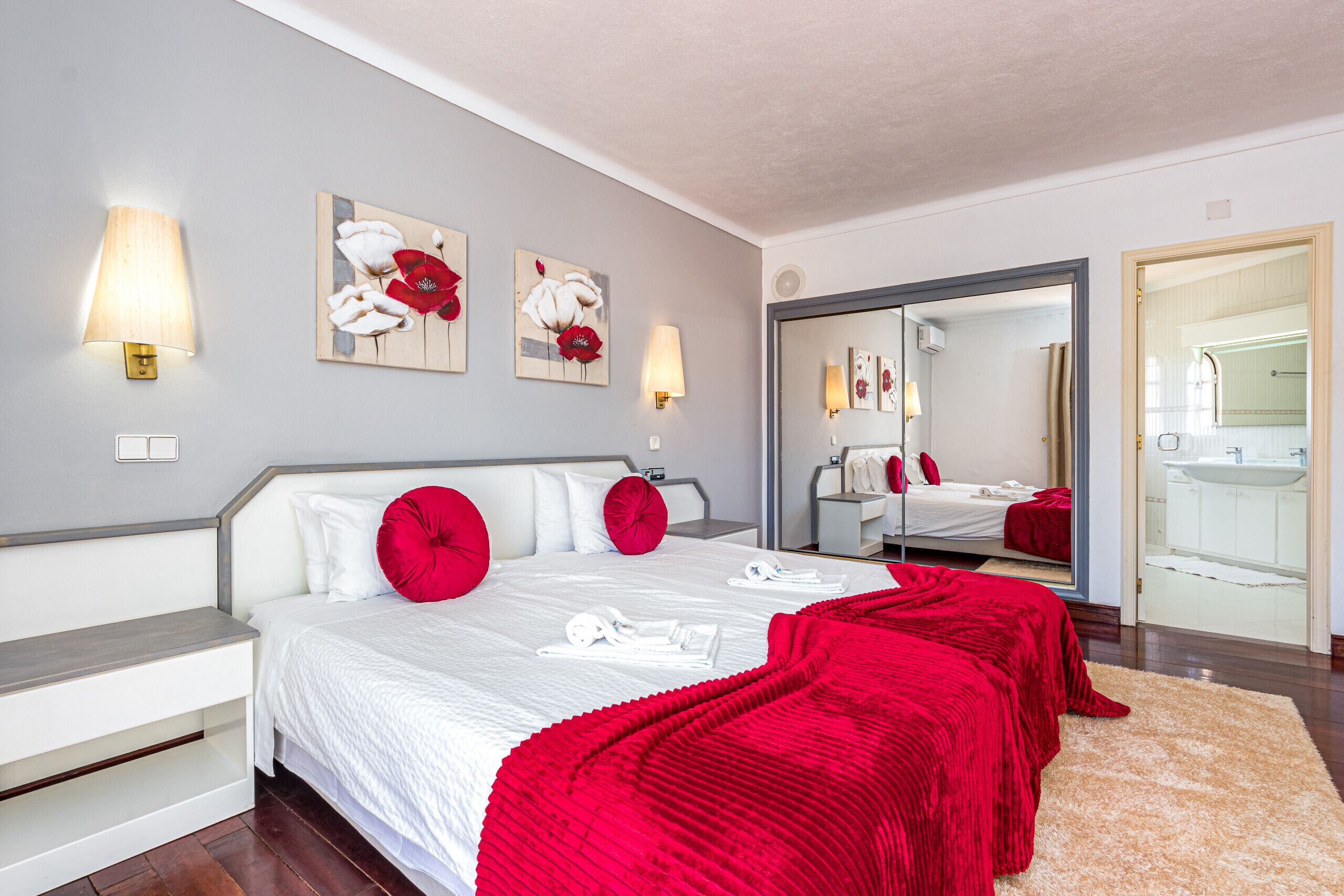 A hotel room with a large bed, red pillows, a white headboard, and artwork on the wall.