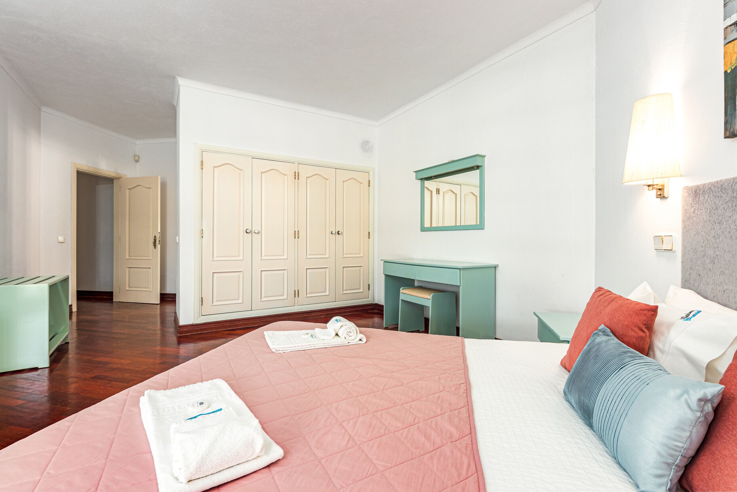 A hotel room with a bed, a desk, a wardrobe, and a mirror.