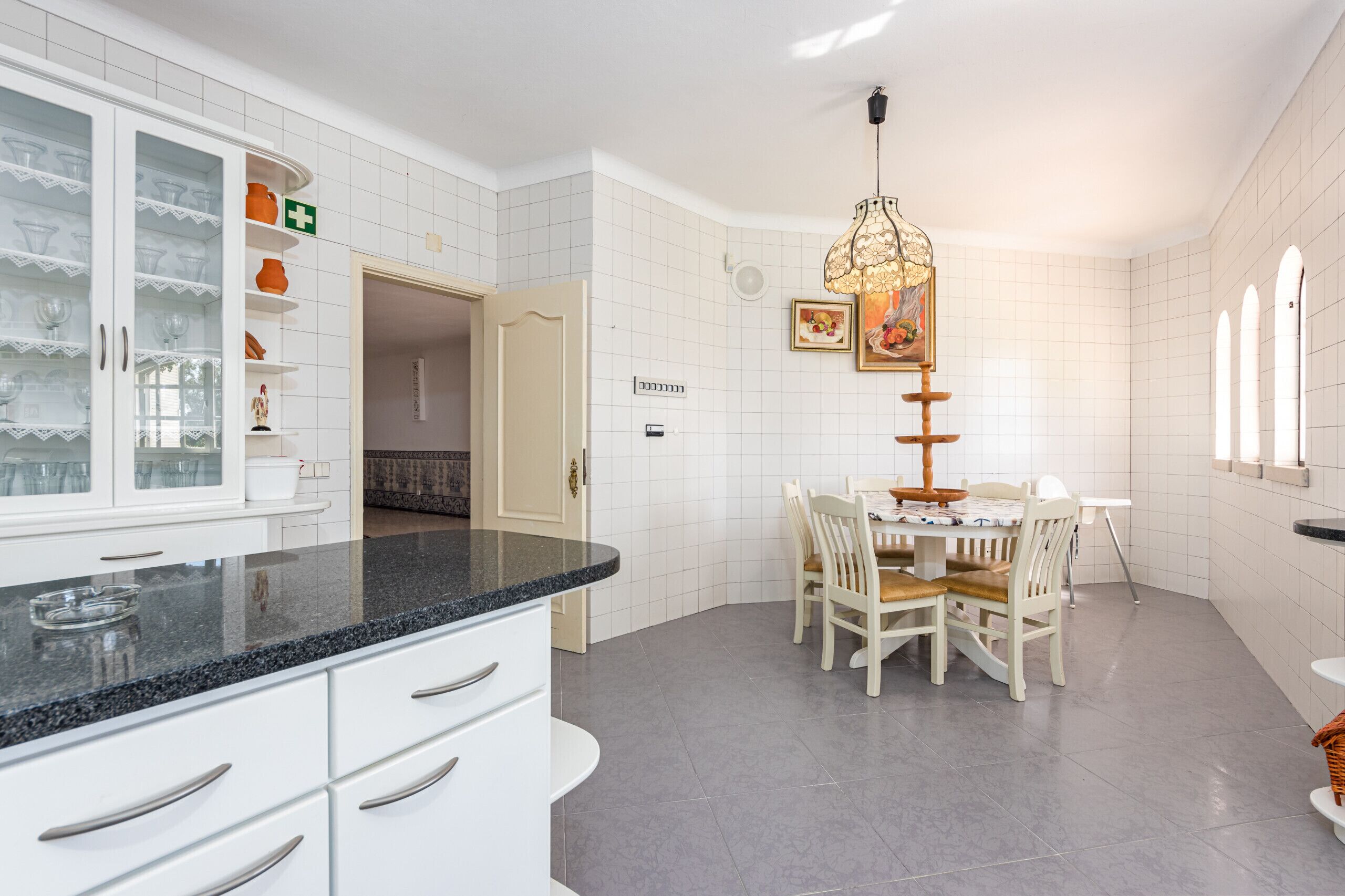 A kitchen with white cabinets, a granite countertop, a dining table with chairs, and a hanging light fixture.