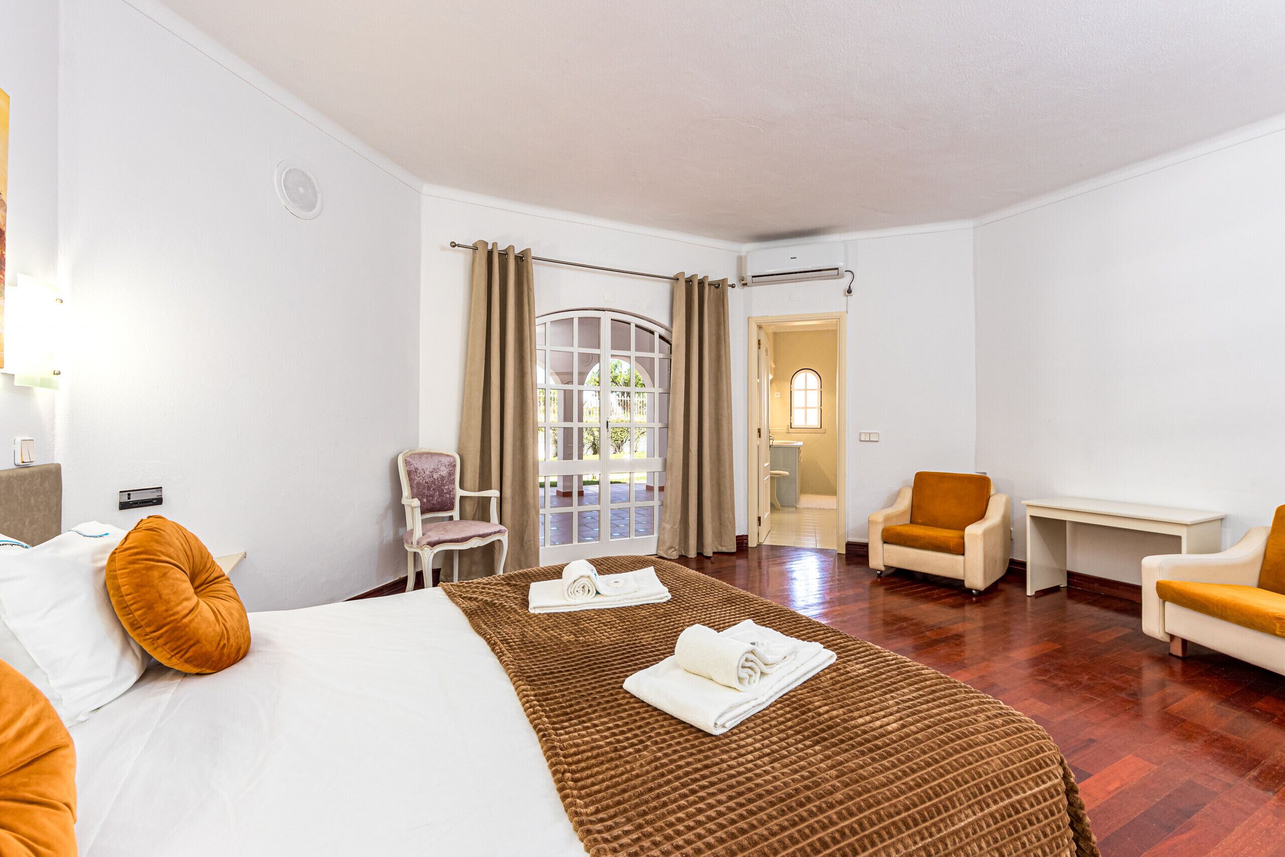 Ein Hotelzimmer mit einem Bett, zwei Sesseln, einem Schreibtisch und Blick ins Freie.