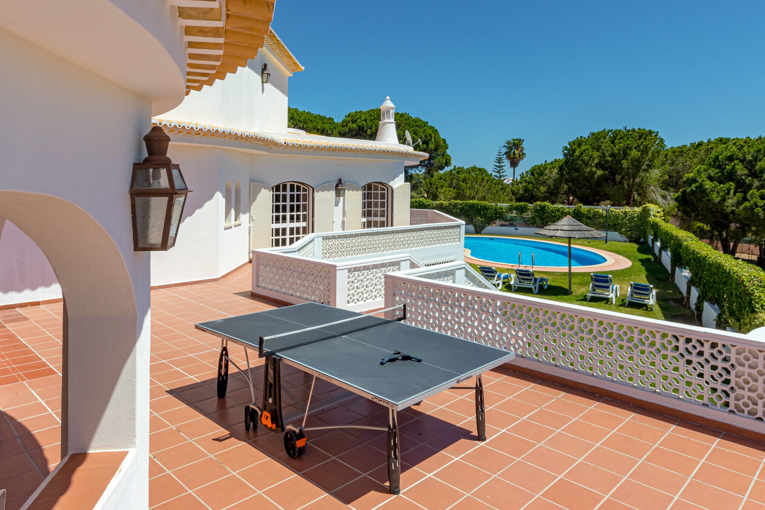 A rooftop terrace with a ping pong table, a swimming pool, and a view of the surrounding greenery.