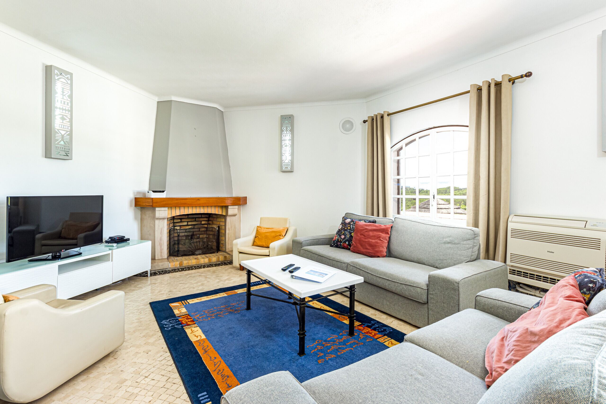 En moderne stue med fjernsyn, pejs, sofa, sofabord og et stort vindue med gardiner.
