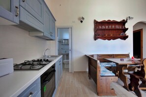A kitchen with a gas stove, cabinets, a sink, and a dining area with a table and benches. - Villa with beautiful sea view (Costa Rei Muravera (CA))