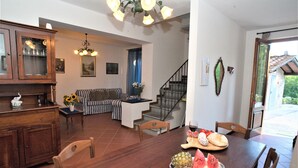 Uma área de refeições com uma mesa de madeira posta para dois, um sofá e uma escada que leva a outro andar.