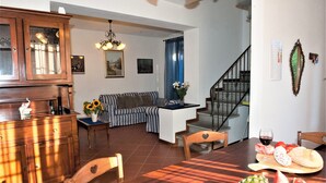 Uma área de refeições com mesa de madeira, cadeiras e um buffet com frutas e pão.