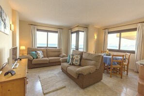 A living room with a sofa, a dining table with chairs, a TV, and a laptop.