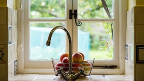A kitchen window with a fruit basket containing apples and peaches, a faucet, and a view of greenery outside. - Characterful Stone Cottage with lovely views over the Surrounding Countryside (Ross-on Wye)