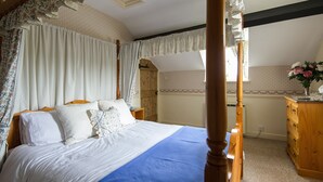 A four-poster bed with white linens and a blue throw blanket, a wooden dresser, and a window with curtains. - Characterful Stone Cottage with lovely views over the Surrounding Countryside (Ross-on Wye)