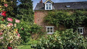 A stone house with a gabled roof, a small dormer window, and a visible chimney. - Characterful Stone Cottage with lovely views over the Surrounding Countryside (Ross-on Wye)