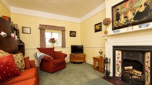 A living room with a fireplace, a television, and a red sofa. - Characterful Stone Cottage with lovely views over the Surrounding Countryside (Ross-on Wye)