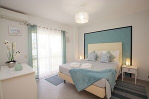 A bedroom with a bed, bedside tables, a lamp, a window with curtains, and a wall-mounted picture.