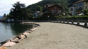 Une plage de sable bordée de pierres, un lac paisible et des maisons en arrière-plan.