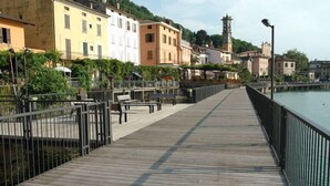 Une promenade en bois, agrémentée de bancs et de garde-corps, qui offre une vue sur une étendue d’eau, avec des bâtiments et une tour en arrière-plan.