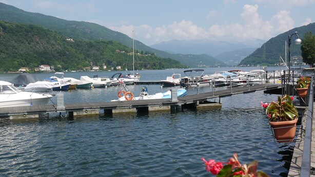 Un port de plaisance où sont amarrés des bateaux, entouré de collines et surplombé d’un ciel dégagé.
