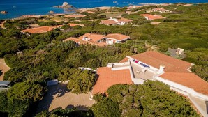 Vue aérienne d’un quartier résidentiel situé sur la côte, avec des maisons aux toits recouverts de tuiles rouges, entourées de verdure et offrant une vue dégagée sur la mer.