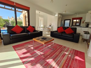 A modern living room with two black sofas, red cushions, a wooden coffee table, and a red patterned rug.