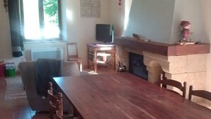 Ein Essbereich mit einem langen Holztisch, Stühlen, einer Couch, einem Fernseher und einem Kamin.