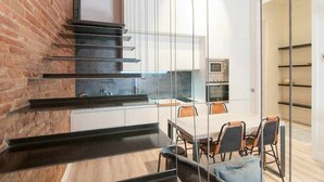 A modern kitchen with a brick wall, a staircase, and a dining area with a table and chairs. - Stylish Apartment C in city center (Barcelona)