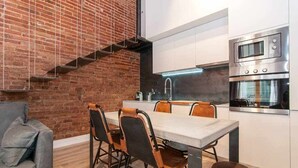 A modern kitchen with a brick wall, stainless steel appliances, and a dining area with a table and chairs. - Stylish Apartment C in city center (Barcelona)