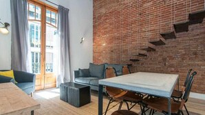 A modern living room with a brick wall, a sofa, a dining table, and a staircase. - Stylish Apartment C in city center (Barcelona)