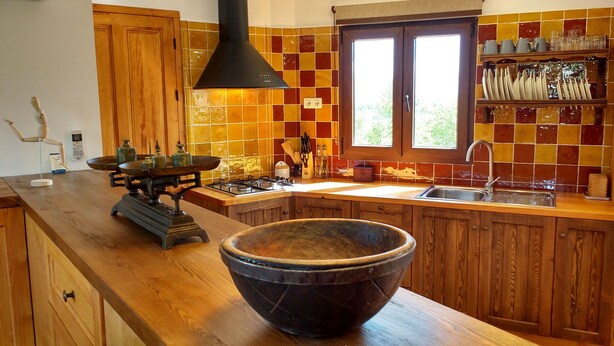 Una cocina con armarios de madera, un tazón negro grande sobre la encimera, una estufa a gas y una ventana con vista a la vegetación.