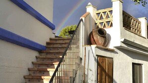 Un edificio blanco con detalles azules, una escalera de madera con barandillas de metal y una gran maceta de barro en el porche.