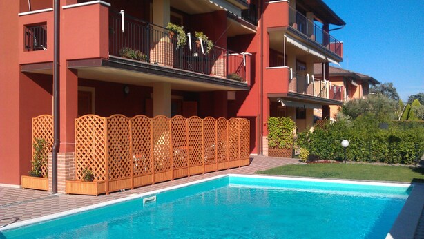 Una piscina con una valla de madera y un edificio con balcones y plantas.