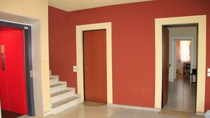 Un pasillo con una puerta roja, paredes color beige y una escalera que sube a un piso superior.