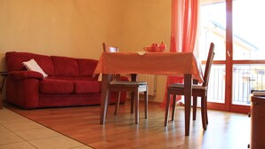 Una sala de estar con un sofá rojo, una mesa de comedor con sillas y una ventana con cortinas.